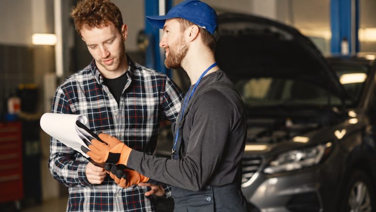 Mecânico conversando com um cliente na oficina, com um carro de capô aberto ao fundo