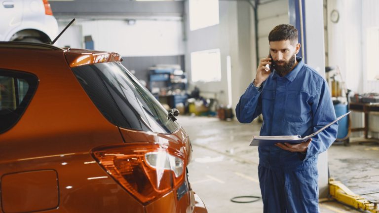 Mecânico falando ao telefone ao lado de um carro na oficina